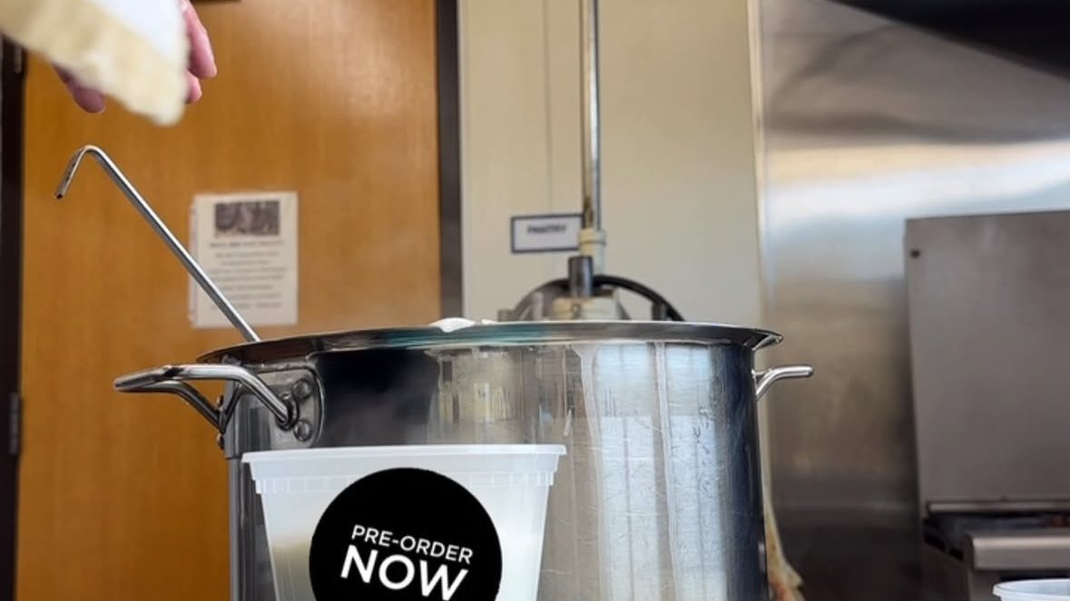 A tall stainless steaming pot in Uncle Mahi's kitchen with a fresh-cut piece of kūlolo held above it and a pre-order note on the container.